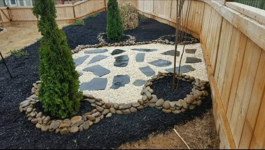 Backyard with dark mulch, new trees, river rocks, pebbles, and pavers.